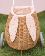 A child happily stood in the sun next to the Olli Ella Rattan Bunny Luggy with Lining – Gumdrop and holding the Rattan basket in Gumdrop