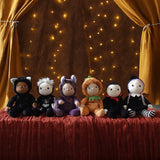 A collection of six Halloween themed Olli Ella dinky dinkums all lined up on a surface covered with a dark red coloured cloth. These soft toys are part of Olli Ella's Halloween collection available here at Babipur.