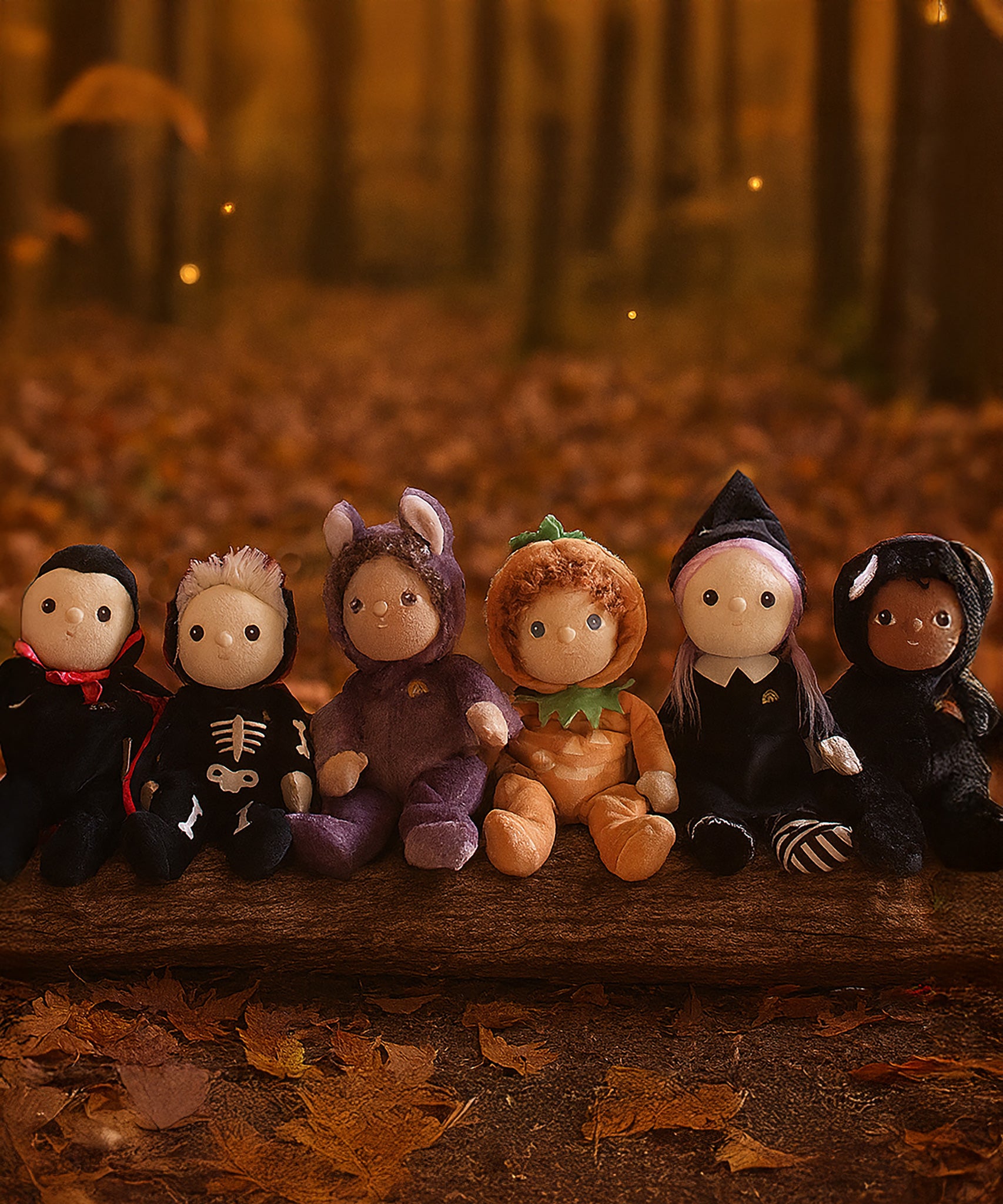 A collection of six Halloween themed Olli Ella dinky dinkums all lined up on a log. These soft toys are part of Olli Ella's Halloween collection available here at Babipur.