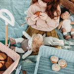 Girl sat down on a blue blanket eating a cake next to the Olli Ella vintage blue wonder wagon
