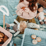 Girl sat down on a blue blanket eating a cake next to the Olli Ella vintage blue wonder wagon