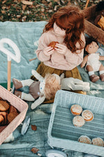Girl sat down on a blue blanket eating a cake next to the Olli Ella vintage blue wonder wagon