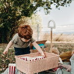 Boy crouched down on a blue blanket pulling popcorn from inside the Olli Ella pink rattan wonder wagon