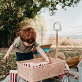 Boy crouched down on a blue blanket pulling popcorn from inside the Olli Ella pink rattan wonder wagon