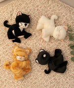 A group of Olli Ella binky kitten toy dolls lying on a floral blanket. These cuddly toys have a sleeping face and feature cute ears and whiskers. These soft dolls are available at Babipur.