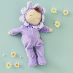 Olli Ella Lavender Pickle Dozy Dinkum Doll laying on a green surface surrounded by little white flower heads. 