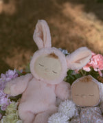 The Olli Ella Pink Bunny Moppet Lullaby Cozy Dinkum placed on a bunch of flowers with another dozy dinkum besides it. 