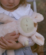 A close up of the Olli Ella Pink Bunny Moppet Lullaby Cozy Dinkum in a child's arms.