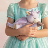 A child wearing a princess outfit and holding a Olli Ella misty binky dragon doll. This light purple fluffy dragon has a sleeping face and features glittery wings and comes with a purple magnetic pacifier. This soft toy is available at Babipur.