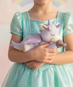 A child wearing a princess outfit and holding a Olli Ella misty binky dragon doll. This light purple fluffy dragon has a sleeping face and features glittery wings and comes with a purple magnetic pacifier. This soft toy is available at Babipur.