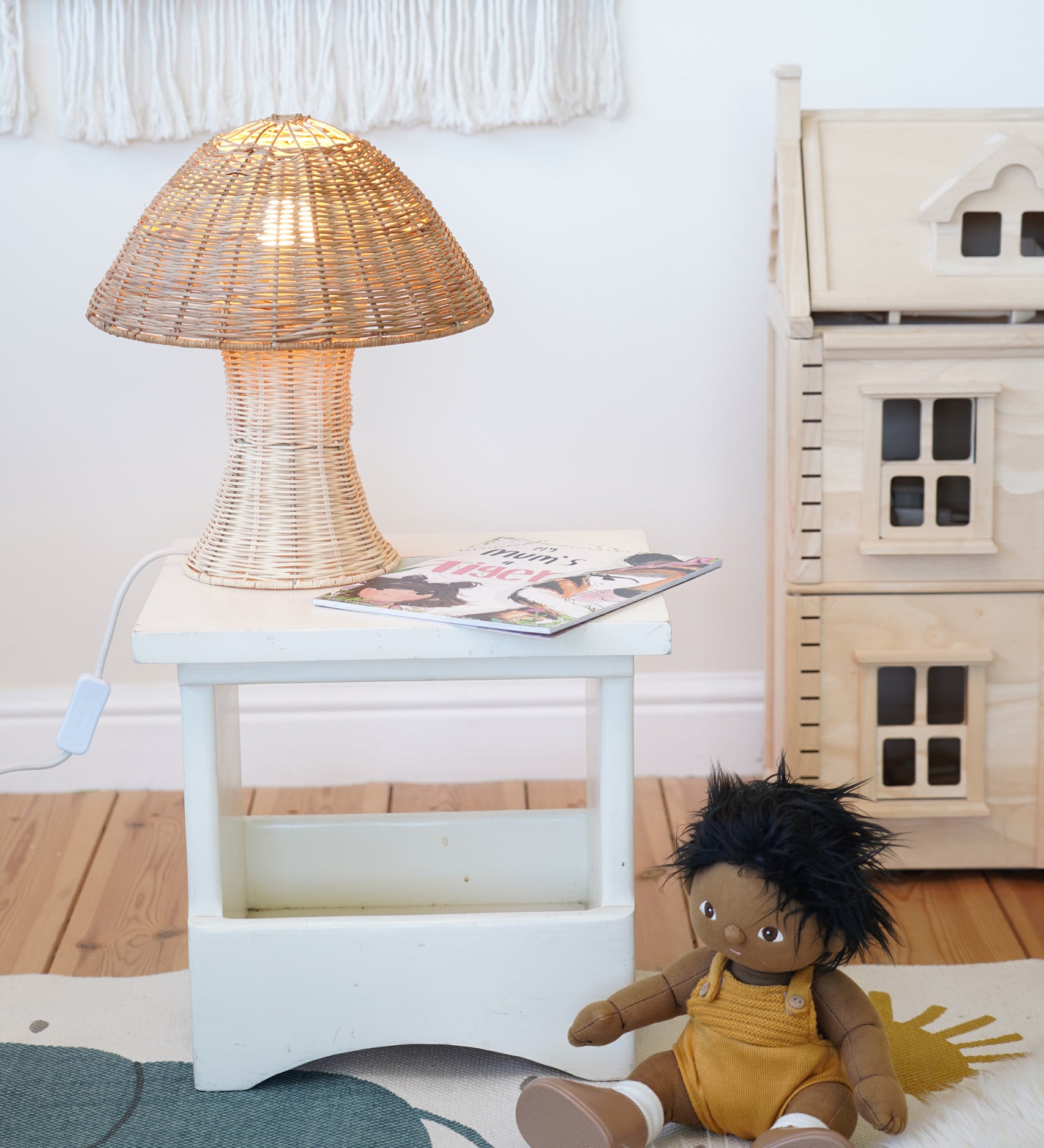 An Olli Ella Natural Rattan Mushroom Lamp placed on a small white square stool.
