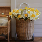 An Olli Ella Natural Rattan Petal Luggy filled with yellow daffodil flowers. 