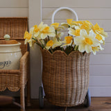 An Olli Ella Natural Rattan Petal Luggy filled with yellow daffodil flowers. 