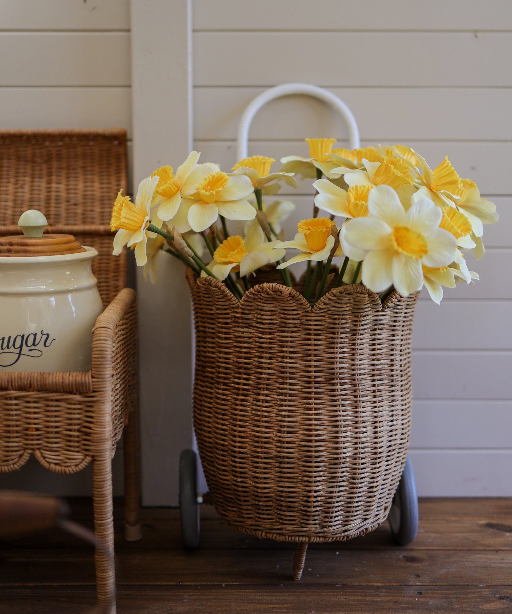 An Olli Ella Natural Rattan Petal Luggy filled with yellow daffodil flowers. 