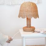 An Olli Ella Rattan Petal Lamp placed on a white bedside table. 