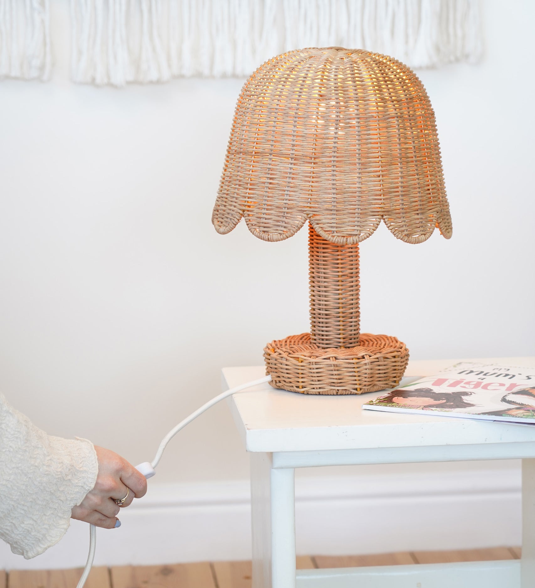 An Olli Ella Rattan Petal Lamp placed on a white bedside table. 