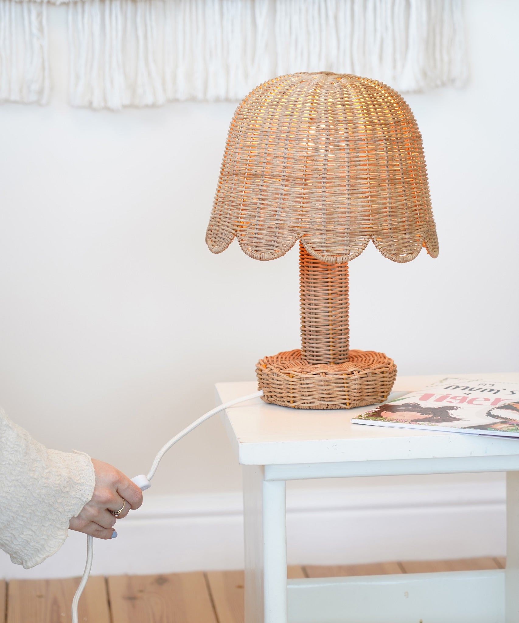 An Olli Ella Rattan Petal Lamp placed on a white bedside table. 