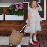 A child wearing a part dress pulling along an Olli Ella Natural Rattan petal luggy. 