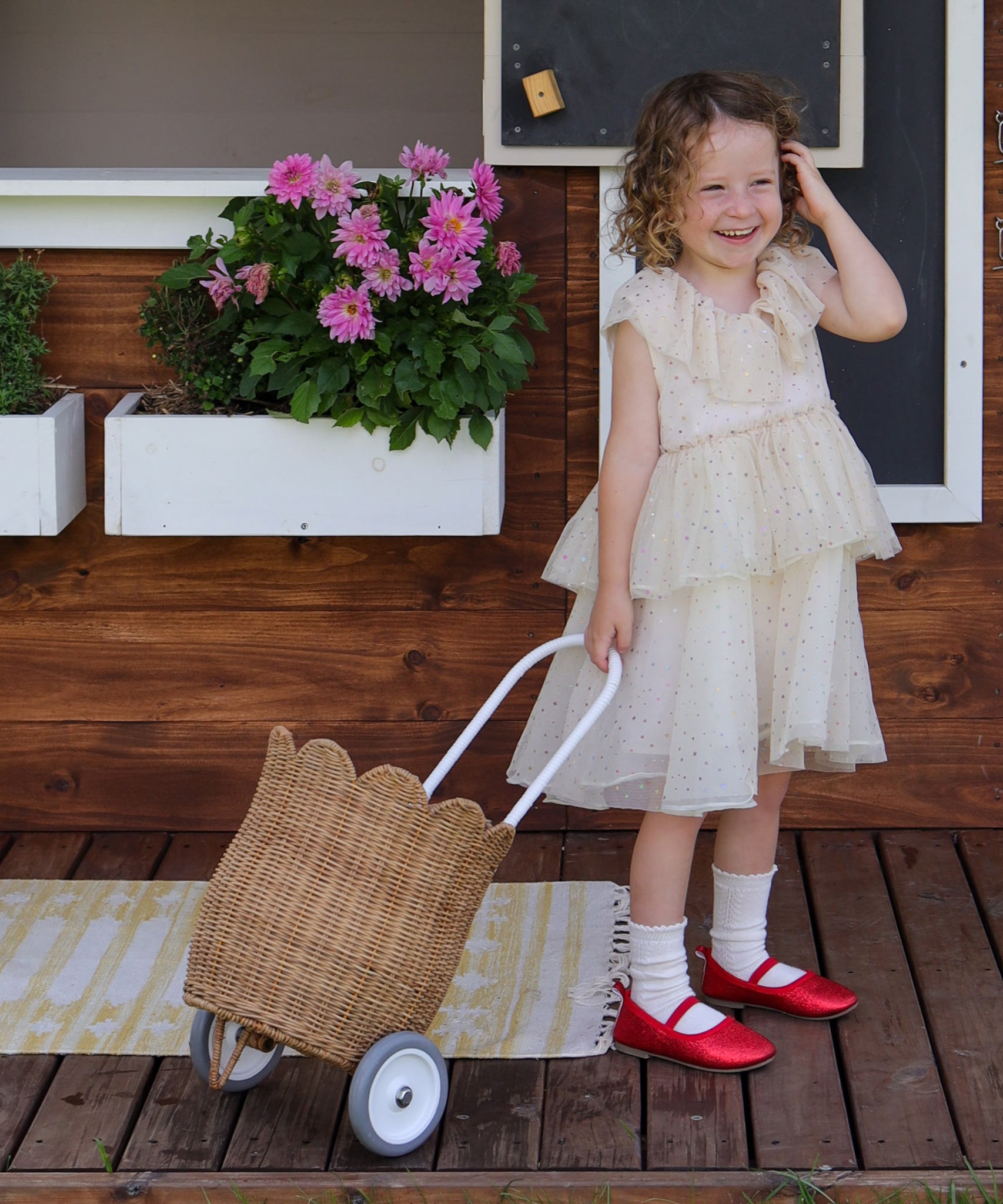A child wearing a part dress pulling along an Olli Ella Natural Rattan petal luggy. 