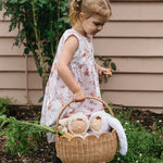 A child carrying a Natural Rattan Olli Ella Petal Basket. There are two bunny dozy dinkums and carrots inside the basket. 