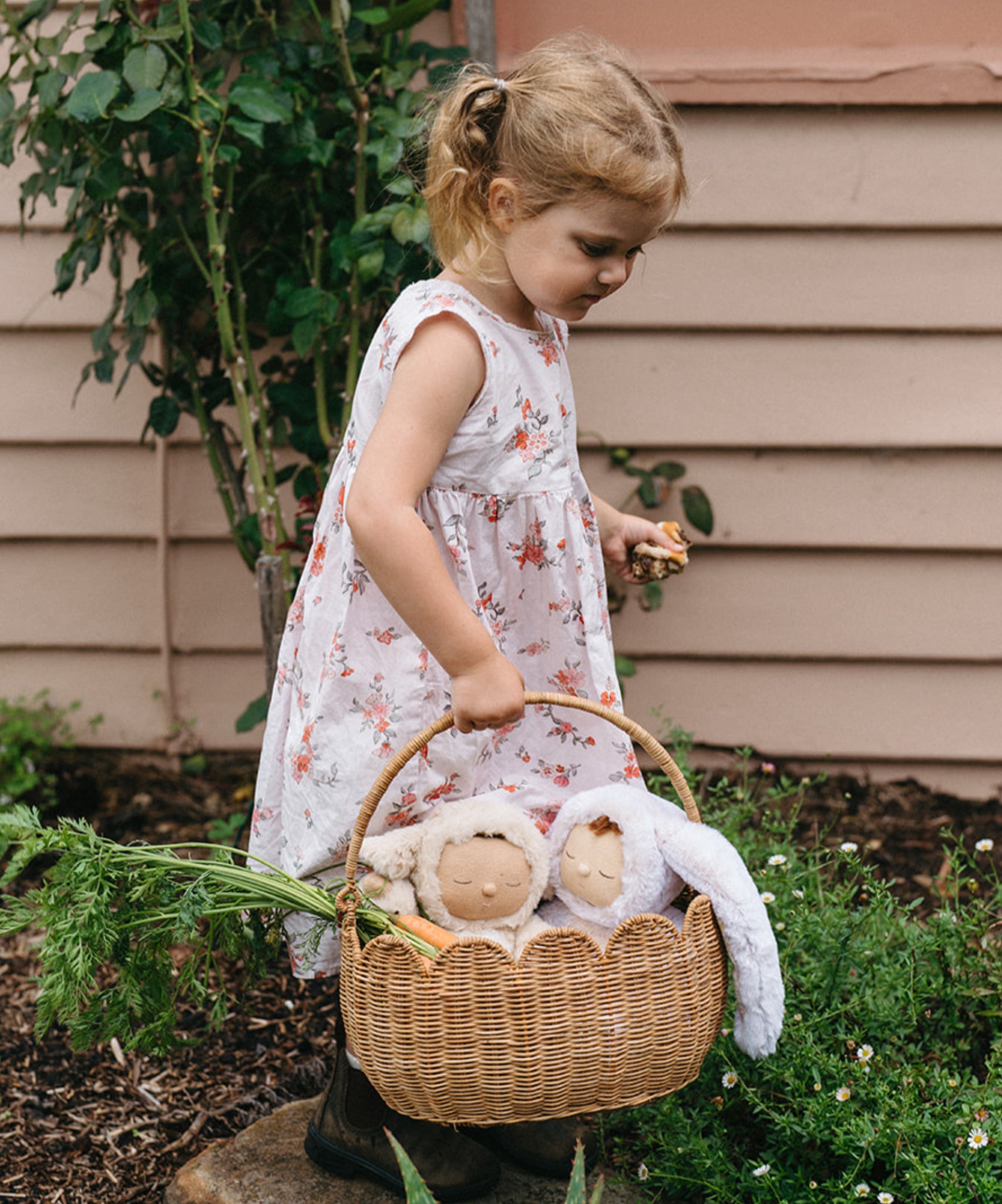 A child carrying a Natural Rattan Olli Ella Petal Basket. There are two bunny dozy dinkums and carrots inside the basket. 