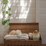 A Olli Ella Natural Petal Storie Bench shown with the lid open. A pile of blankets and a Dozy Dinkum can be seen inside with some cups and crockery storage pots. 