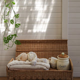 A Olli Ella Natural Petal Storie Bench shown with the lid open. A pile of blankets and a Dozy Dinkum can be seen inside with some cups and crockery storage pots. 