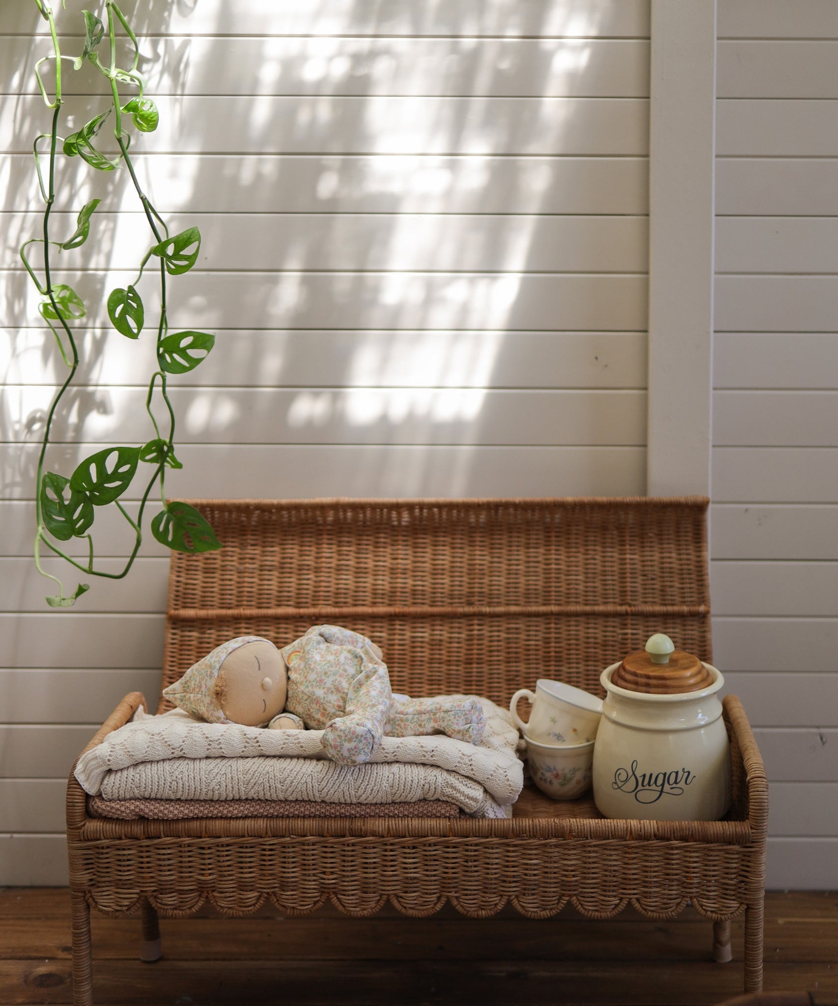 A Olli Ella Natural Petal Storie Bench shown with the lid open. A pile of blankets and a Dozy Dinkum can be seen inside with some cups and crockery storage pots. 
