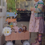 A child pushing a Seashell Pink Olli Ella Petal Wonder Wagon along in front of them. The wagon is filled with Dinky Dinkums and a bunch of white flowers. 