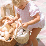 A child collecting eggs from a colourful blanket and into the Olli Ella Rattan Berry Basket with Lining – Pansy Floral.