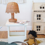 An Olli Ella Rattan Petal Lamp placed on a white bedside table. 