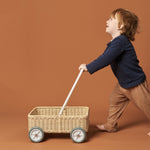 Young boy pushing the Olli Ella handmade rattan Wamble Walker on a brown background