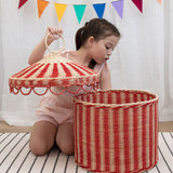A child lifting the lid off the Olli Ella Red & Straw Rattan Circus Tent Basket. This large capacity basket is perfect for use as toy storage. Olli Ella have a range of stylish storage solutions and soft toys available here at Babipur. 