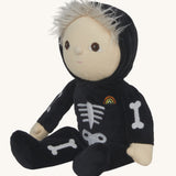 Olli Ella Scully Skeleton Dinky Dinkum Doll soft toy in a sitting position. The doll features glow in the dark bone details on the front along with a small embroidered rainbow on the chest. These soft toys are part of Olli Ella's Halloween collection available here at Babipur.