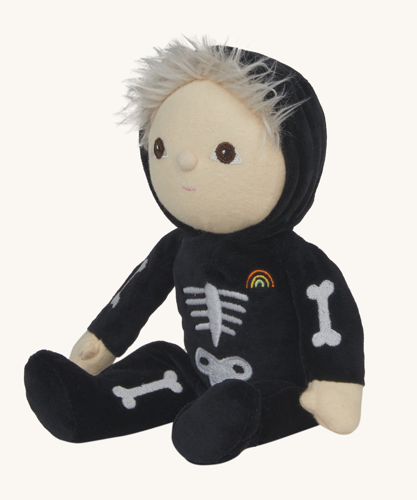 Olli Ella Scully Skeleton Dinky Dinkum Doll soft toy in a sitting position. The doll features glow in the dark bone details on the front along with a small embroidered rainbow on the chest. These soft toys are part of Olli Ella's Halloween collection available here at Babipur.