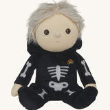 Olli Ella Scully Skeleton Dinky Dinkum Doll soft toy shown with it's hood down, the doll has light blonde hair. The doll features glow in the dark bone details on the front along with a small embroidered rainbow on the chest. These soft toys are part of Olli Ella's Halloween collection available here at Babipur.
