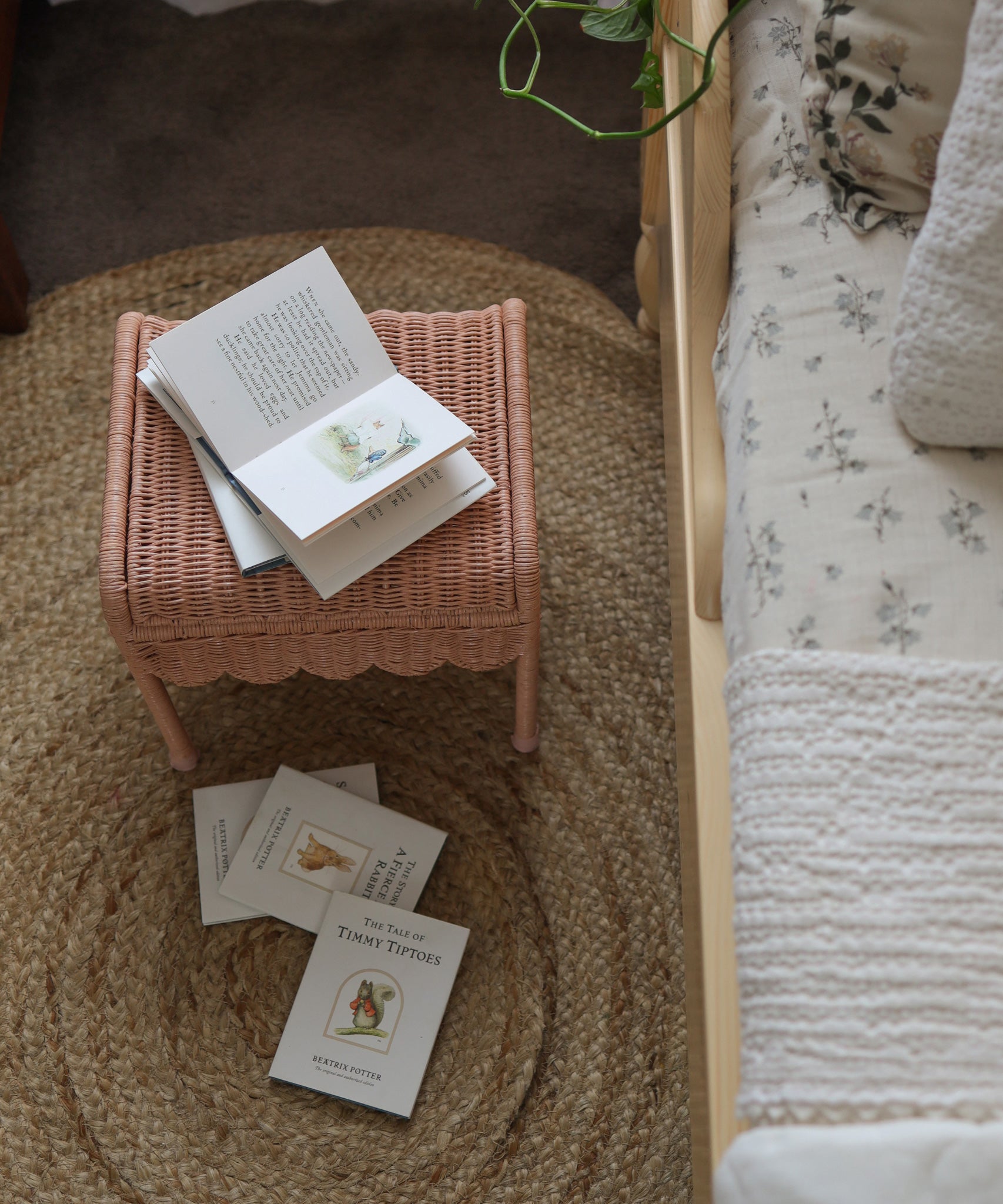 Olli Ella Petal Storie Stool in Seashell Pink Rattan. The stool is shown next to a bed with books placed on top
