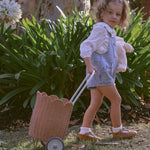 A child pulling along a Olli Ella Seashell Pink Rattan Petal Luggy.