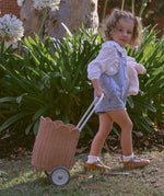 A child pulling along a Olli Ella Seashell Pink Rattan Petal Luggy.