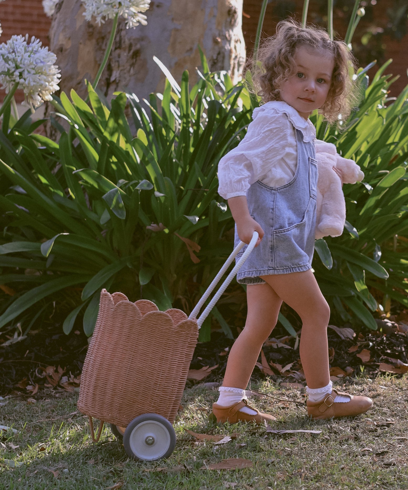 A child pulling along a Olli Ella Seashell Pink Rattan Petal Luggy.