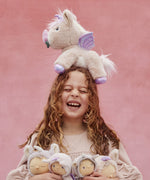 A girl with the Olli Ella Dinkum unicorn balancing on her head, and holding lots of dinky dinkums in her arms