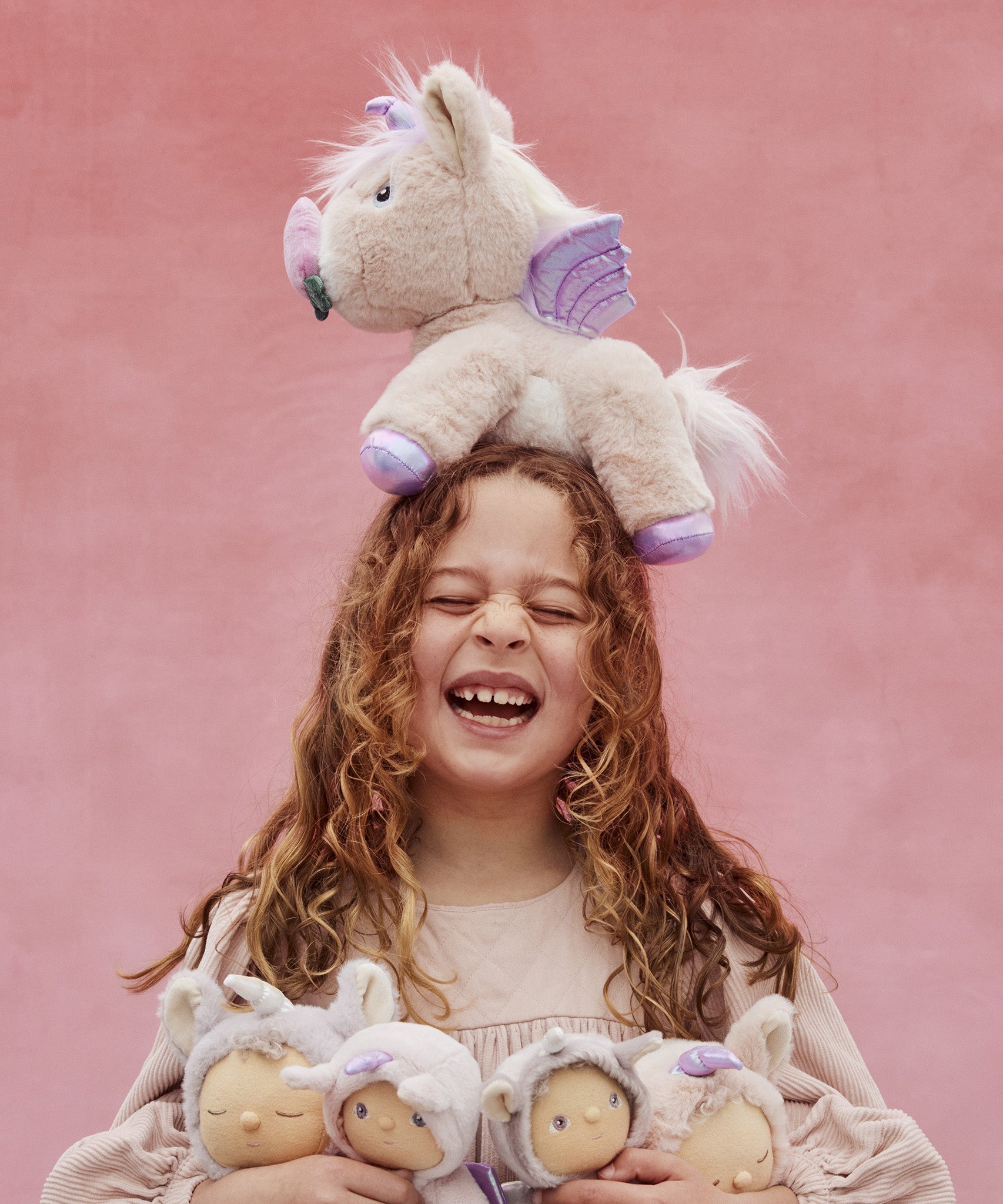 A girl with the Olli Ella Dinkum unicorn balancing on her head, and holding lots of dinky dinkums in her arms