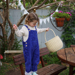 A child holding the Straw Olli Ella Rattan Gathering basket. The child is standing on a wooden bench. 
