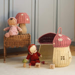 The Olli Ella Rattan Woven mushroom doll's house, with a pink spotty toadstool top and an opening door. Next to it are two toadstool dozy dinkum dolls and some toys. 