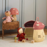 The Olli Ella Rattan Woven mushroom doll's house, with a pink spotty toadstool top and an opening door. Next to it are two toadstool dozy dinkum dolls and some toys. 