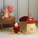 The Olli Ella Rattan Woven mushroom doll's house, with a red spotty toadstool top and an opening door. Next to it are two toadstool dozy dinkum dolls and some toys. 