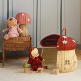 The Olli Ella Rattan Woven mushroom doll's house, with a red spotty toadstool top and an opening door. Next to it are two toadstool dozy dinkum dolls and some toys. 