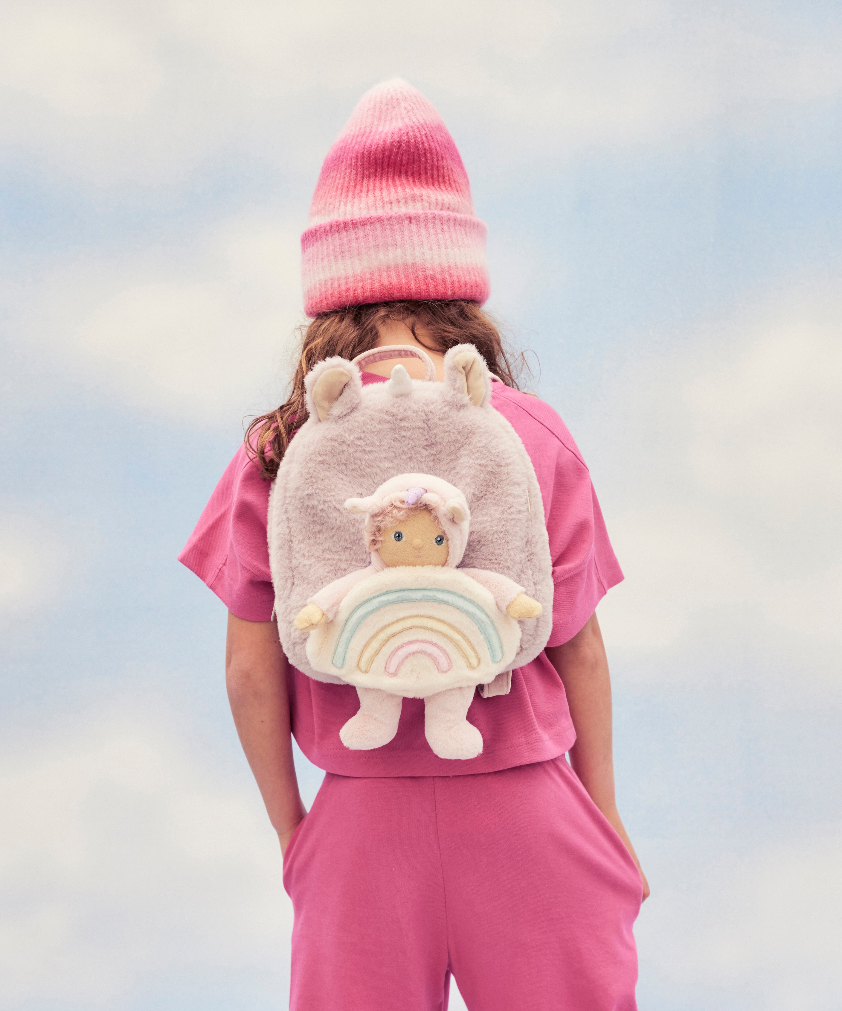A child wearing the pink fluffy Olli Ella backpack with a dinky dinkum doll sitting in the bag.