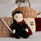 An Olli Ella Vincent Vampire Dinky Dinkum doll placed in a seated position in front of baskets. A soft vampire doll with a black cape with bat shaped glow in the dark details on the back. These soft toys are part of Olli Ella's Halloween collection available here at Babipur.
