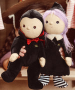 A child holding an Olli Ella Vincent Vampire Dinky Dinkum doll and a Willa Witch doll in their hand. Each doll has some glow in the dark features. These soft toys are part of Olli Ella's Halloween collection available here at Babipur.